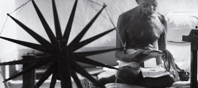 Mahatma Gandhi llegint al costat de la seva màquina de teixir.